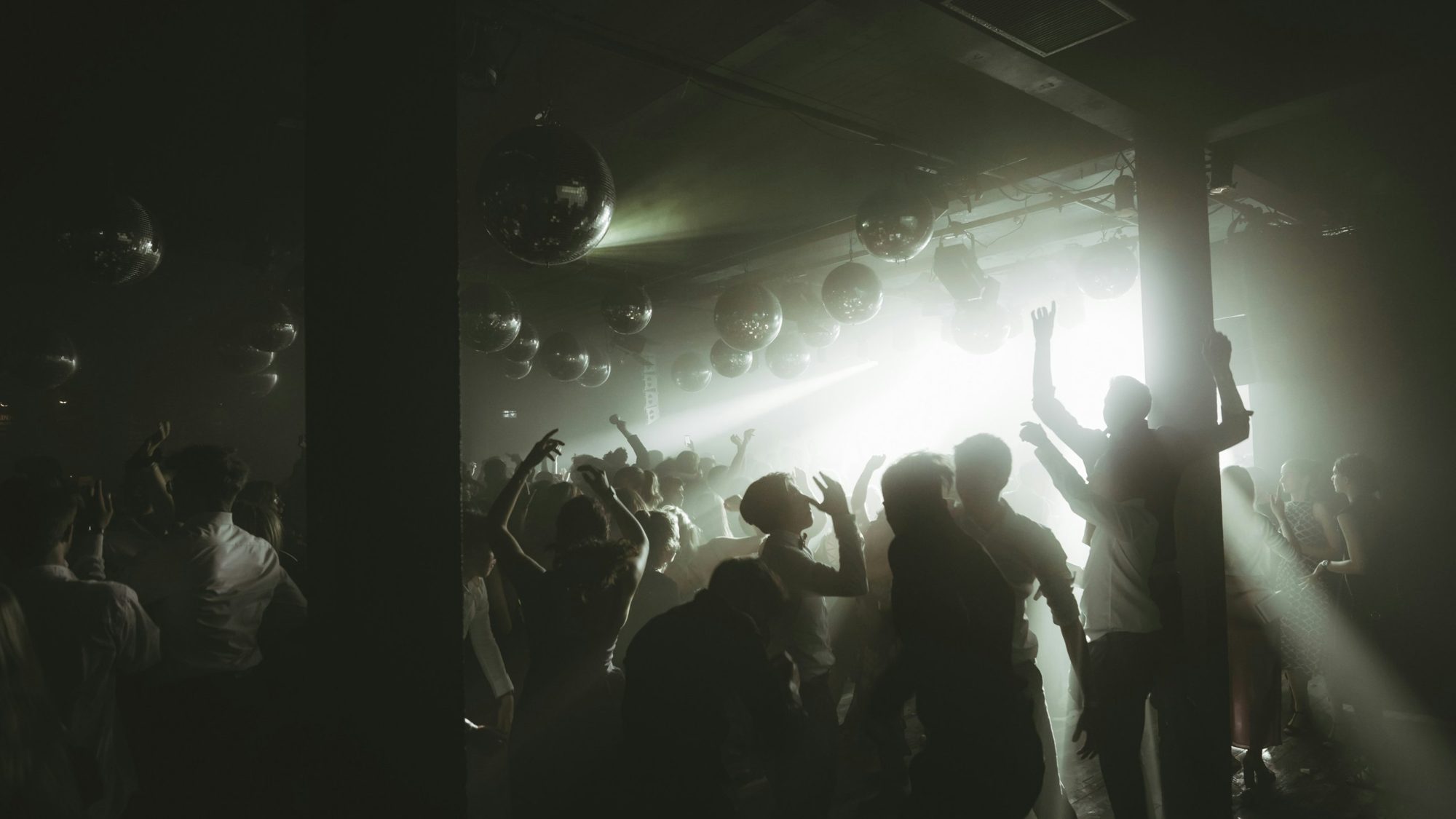 Tanzende Menge auf einer Abiparty unter Discokugeln im Gegenlicht