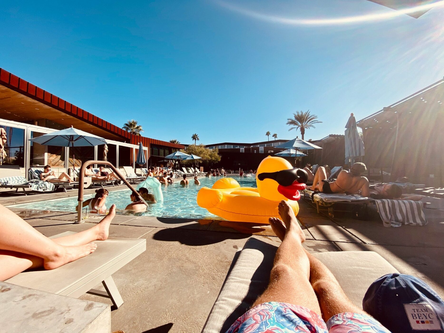 Abireise am Pool, Blick über eine gelbe Badeente auf die Liegen in der Sonne
